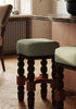 Pair of wooden stools with green cushioned seats in a room with a lamp and window.